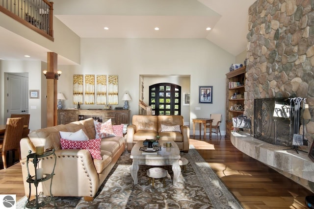 living room featuring high vaulted ceiling, a stone fireplace, and dark wood-type flooring