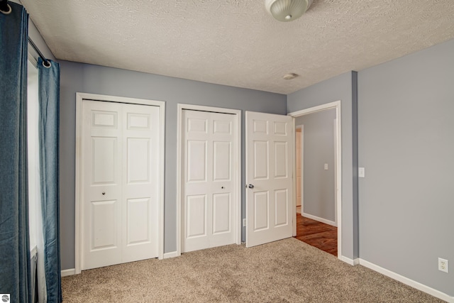 unfurnished bedroom with two closets, carpet, and a textured ceiling