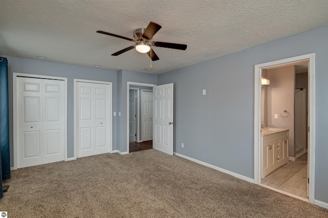 unfurnished bedroom with ensuite bathroom, ceiling fan, a textured ceiling, light colored carpet, and multiple closets