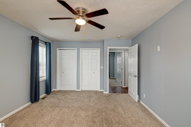 unfurnished bedroom featuring a textured ceiling, carpet floors, ceiling fan, and multiple closets