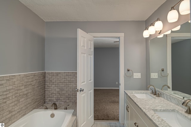 bathroom with a bathing tub, tile walls, vanity, and a textured ceiling