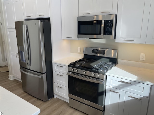 kitchen featuring white cabinetry, light stone counters, light hardwood / wood-style flooring, and appliances with stainless steel finishes