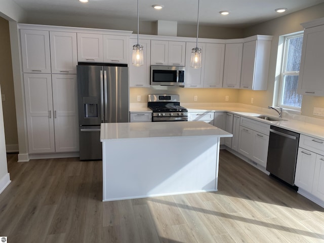 kitchen featuring appliances with stainless steel finishes, sink, pendant lighting, wood-type flooring, and a kitchen island