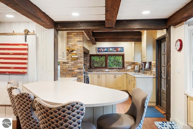 kitchen with beam ceiling, sink, kitchen peninsula, cream cabinetry, and a breakfast bar area