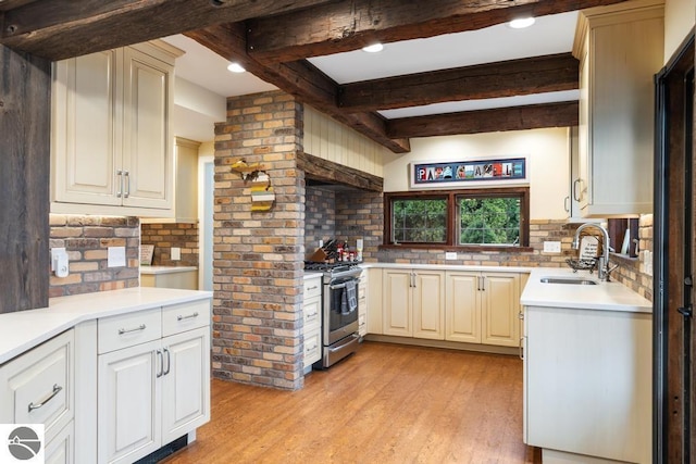 kitchen featuring beamed ceiling, light wood-type flooring, stainless steel gas range oven, and sink