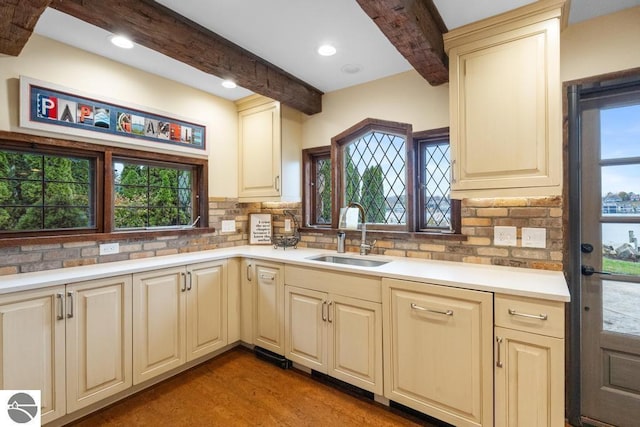 kitchen featuring beam ceiling, sink, tasteful backsplash, cream cabinets, and hardwood / wood-style flooring