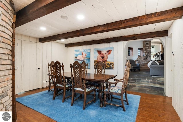 dining room with beam ceiling, ornate columns, wooden walls, and dark wood-type flooring