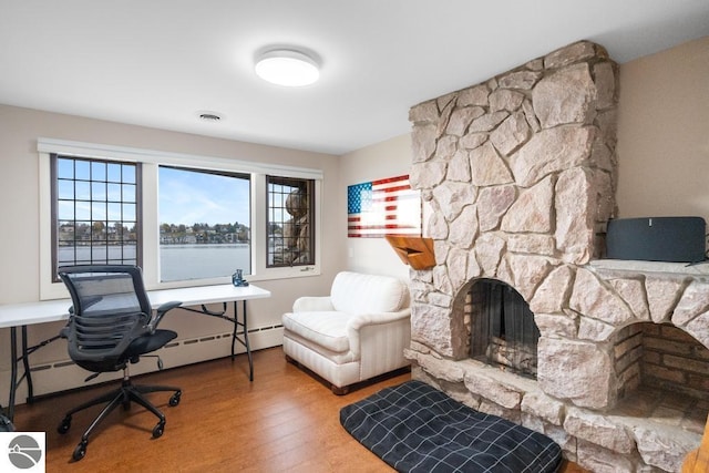 office area featuring a stone fireplace, a water view, and wood-type flooring