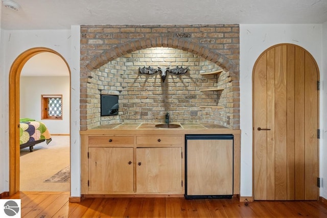 bar with tile countertops, light brown cabinets, stainless steel refrigerator, and light hardwood / wood-style flooring