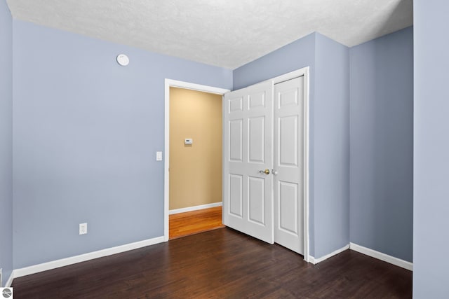 unfurnished bedroom with a textured ceiling, dark hardwood / wood-style flooring, and a closet