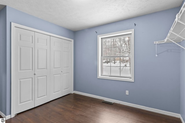 unfurnished bedroom featuring a textured ceiling, a closet, and dark wood-type flooring