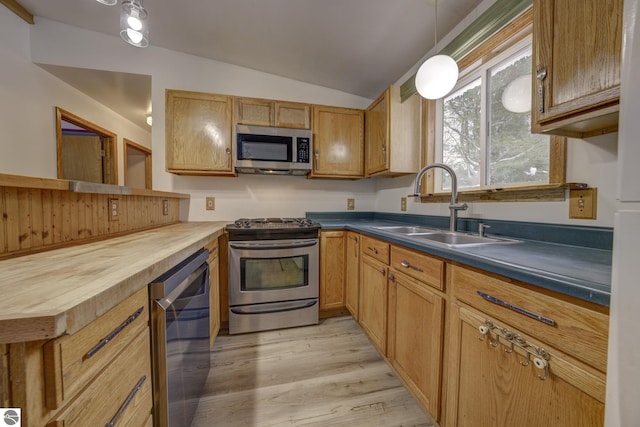 kitchen with stainless steel appliances, sink, pendant lighting, light hardwood / wood-style flooring, and lofted ceiling