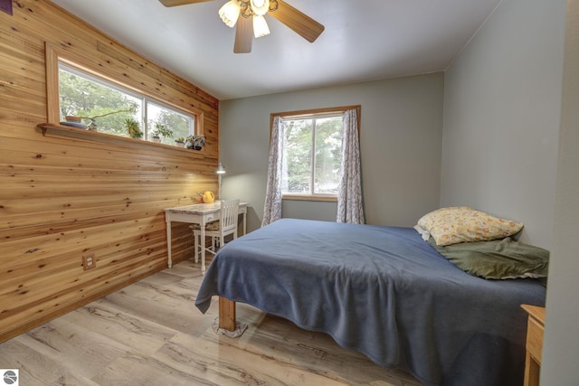 bedroom with light wood-type flooring, ceiling fan, and wooden walls