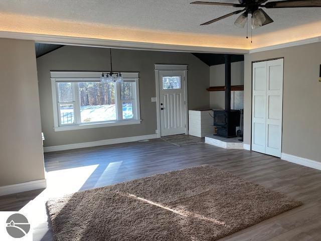 foyer with a textured ceiling, a wood stove, dark wood-type flooring, and ceiling fan with notable chandelier