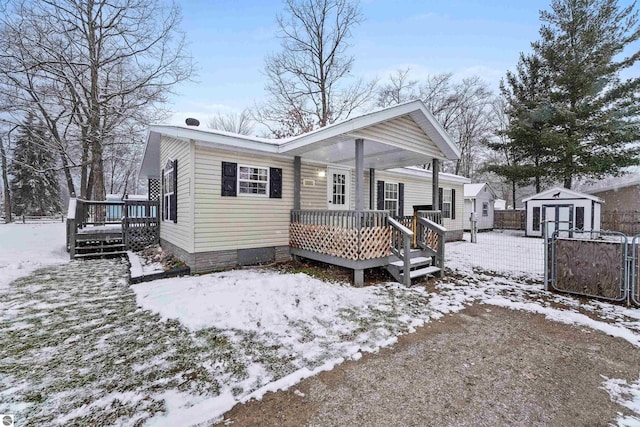 snow covered rear of property featuring a storage unit and a wooden deck