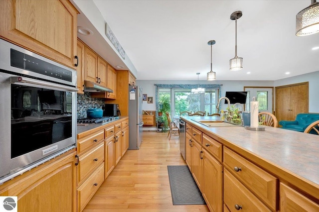 kitchen with appliances with stainless steel finishes, decorative light fixtures, tasteful backsplash, sink, and light wood-type flooring