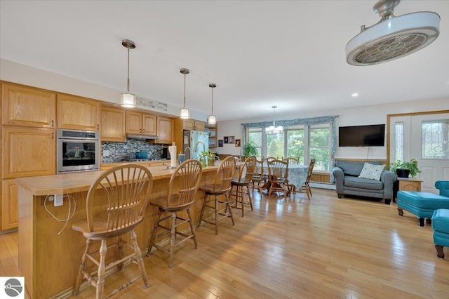 kitchen with a kitchen island with sink, backsplash, stainless steel appliances, light hardwood / wood-style floors, and decorative light fixtures