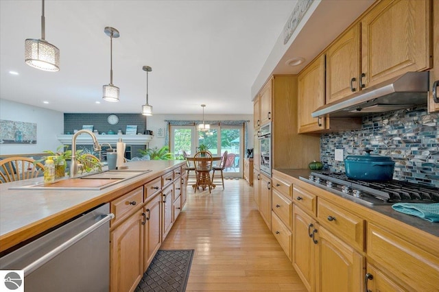 kitchen featuring sink, tasteful backsplash, decorative light fixtures, appliances with stainless steel finishes, and light hardwood / wood-style floors