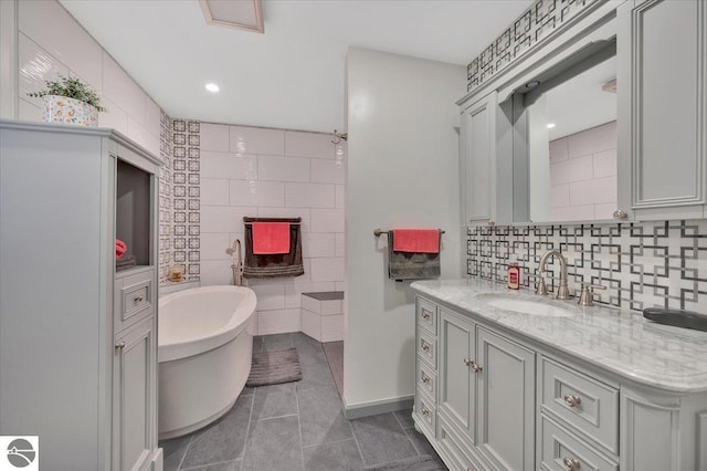 bathroom with tile walls, tile patterned flooring, vanity, tasteful backsplash, and a bathing tub