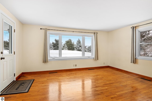 empty room featuring wood finished floors, visible vents, and baseboards