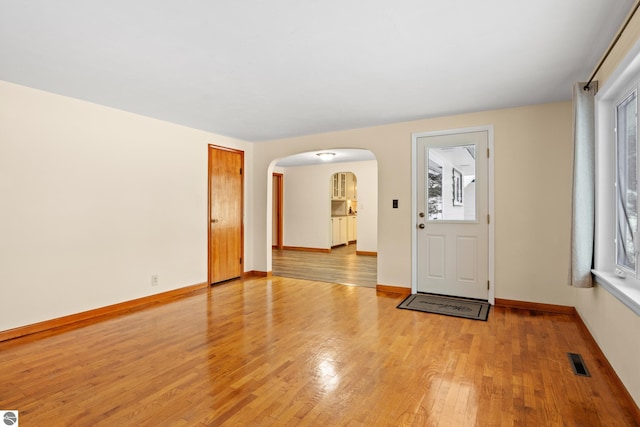 foyer entrance featuring arched walkways, baseboards, visible vents, and light wood-style floors