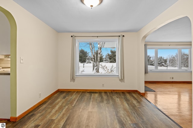 empty room featuring baseboards, arched walkways, and wood finished floors