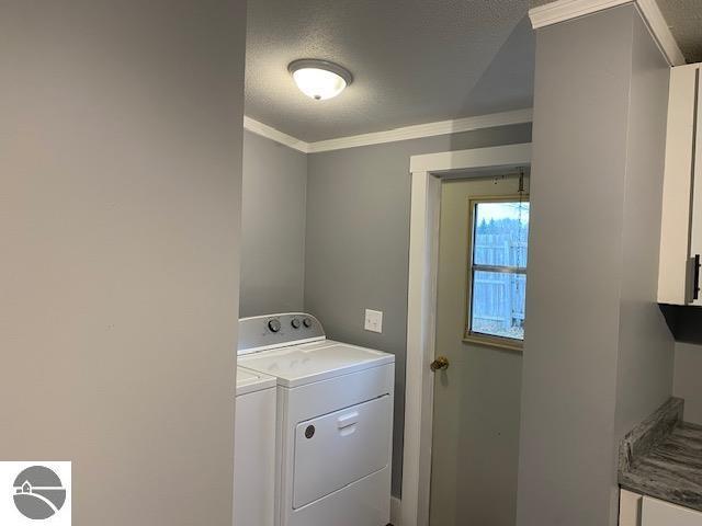 clothes washing area featuring a textured ceiling, washer and dryer, and crown molding