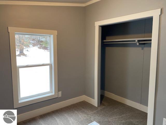 unfurnished bedroom with carpet flooring, a closet, and ornamental molding