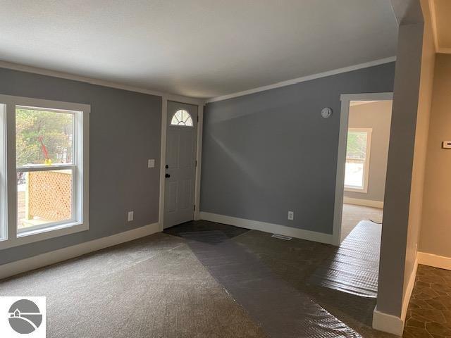 entrance foyer with dark colored carpet, ornamental molding, and vaulted ceiling