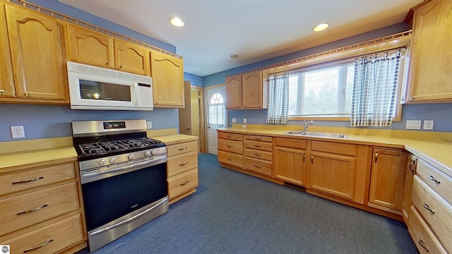 kitchen featuring light brown cabinetry, sink, dark carpet, and stainless steel range with gas stovetop