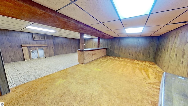 basement featuring light colored carpet, a drop ceiling, and wood walls