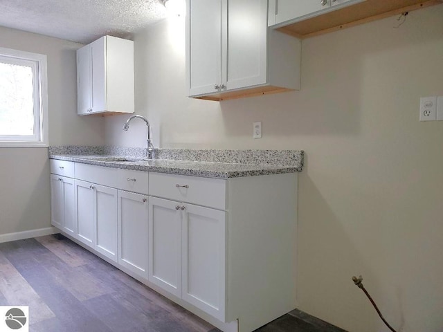 kitchen with light stone countertops, a textured ceiling, sink, light hardwood / wood-style flooring, and white cabinetry