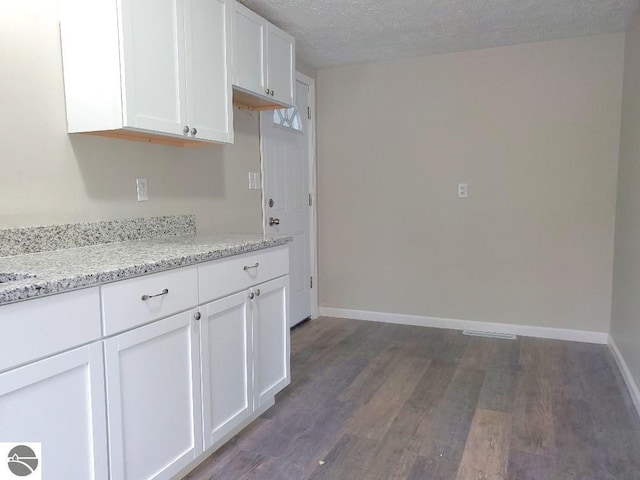 kitchen featuring a textured ceiling, light stone countertops, white cabinetry, and dark wood-type flooring