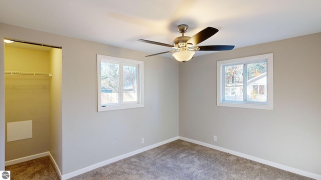 unfurnished bedroom featuring a walk in closet, carpet floors, multiple windows, and ceiling fan