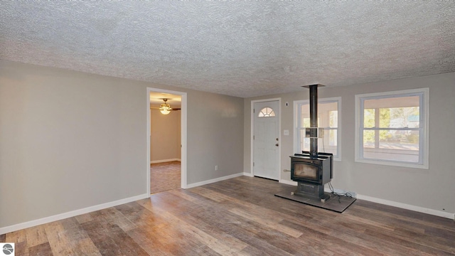 unfurnished living room with a wood stove, ceiling fan, wood-type flooring, and a textured ceiling