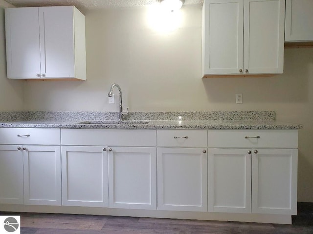 kitchen featuring light stone counters, a textured ceiling, sink, hardwood / wood-style flooring, and white cabinets