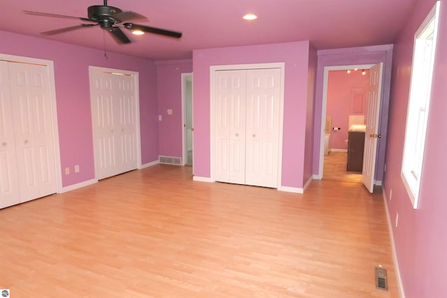 unfurnished bedroom with ceiling fan, light wood-type flooring, and two closets