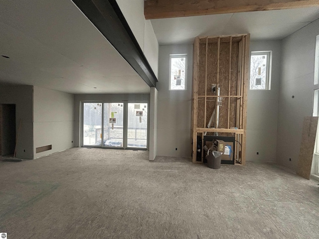 unfurnished living room featuring beamed ceiling, plenty of natural light, and carpet floors