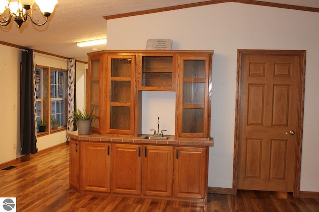kitchen with crown molding, a sink, a chandelier, tile countertops, and dark wood-type flooring