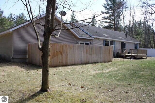 rear view of property featuring a wooden deck, a yard, and fence