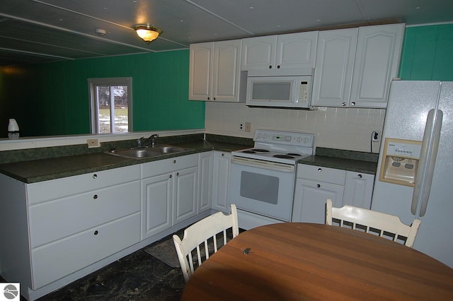 kitchen with wood walls, white appliances, backsplash, white cabinets, and sink