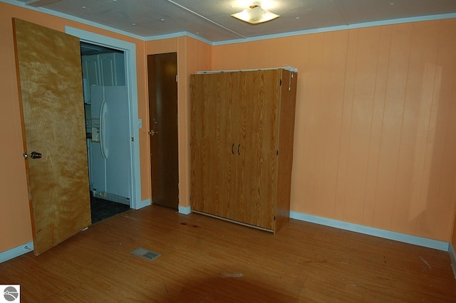 empty room with wood-type flooring, ornamental molding, and wooden walls