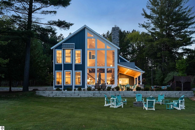 back house at dusk with an outdoor fire pit and a lawn