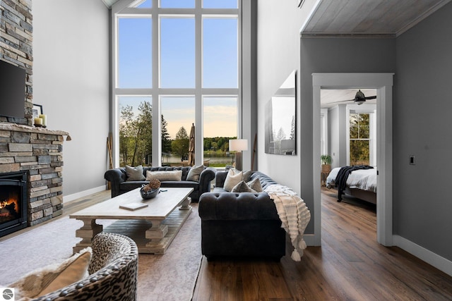 living room featuring a towering ceiling, dark hardwood / wood-style flooring, ornamental molding, ceiling fan, and a stone fireplace