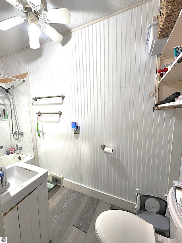 bathroom featuring hardwood / wood-style floors, bathtub / shower combination, wooden walls, ceiling fan, and toilet