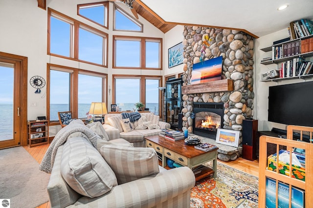 living room featuring a fireplace, high vaulted ceiling, a water view, and light hardwood / wood-style flooring