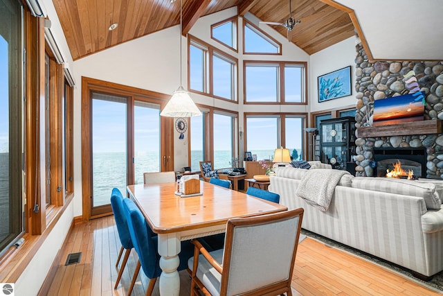 dining room featuring light wood-type flooring, ceiling fan, a water view, high vaulted ceiling, and a fireplace