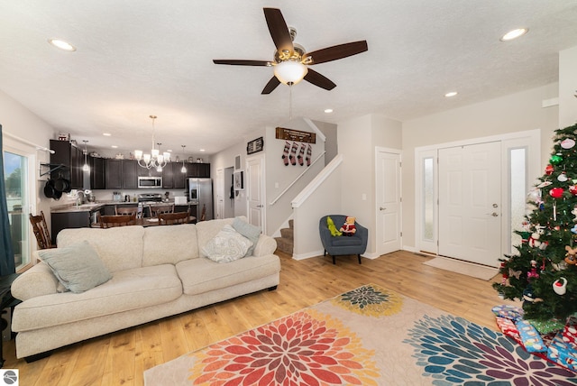 living room with ceiling fan with notable chandelier, sink, a textured ceiling, and light hardwood / wood-style flooring