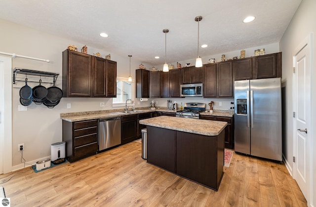 kitchen with sink, light hardwood / wood-style floors, decorative light fixtures, a kitchen island, and stainless steel appliances