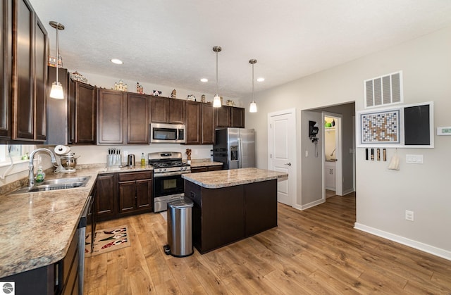 kitchen with a center island, stainless steel appliances, decorative light fixtures, and light wood-type flooring